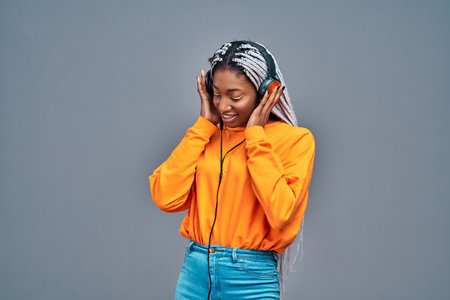 Adorable afro american woman in yellow shirt singing and having fun while listening to music using...