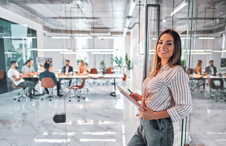 Woman standing with laptop in a modern bright office. Businesswoman with laptop by glass wal of new office. Front viewの写真素材
