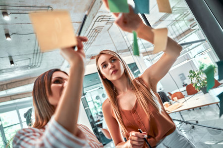 Confident and smart. Group of young modern people in smart casual wear using adhesive notes while...