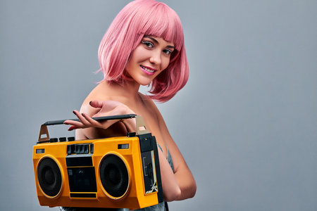 Young woman in a pink wig holding yellow record-played, isolated on gray background. Copy spaceの写真素材
