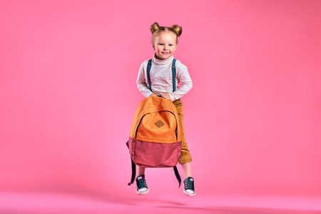 Funny little girl with big backpack jumping and having fun against pink wall. School concept. Back to School. School's out for summer. Celebrating the end of another successful school year. Copy spaceの写真素材
