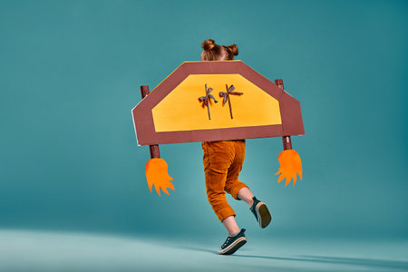 Happy child playing. Kid having fun intdoors. Kid holding cardboard wings. Travel and vacation concept. Imagination and freedom concept. Back view. Isolated blue background. Copy spaceの写真素材