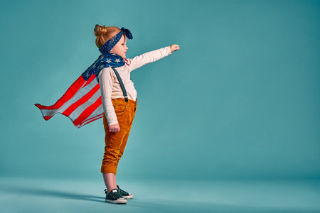 Happy independence day. Little smiling patriotic girl with an american flag waving in the wind on blue background. Copy spaceの写真素材