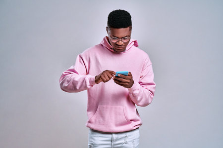 Portrait of an excited young afro american man dressed in hoodie isolated, holding mobile phone. Copy spaceの写真素材