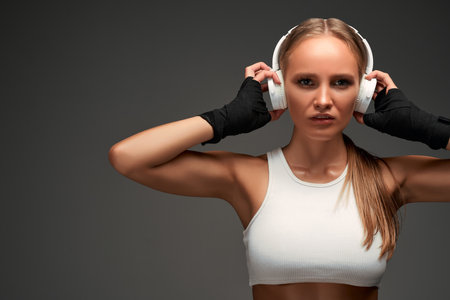 Favorite playlist. Young sporty african sporty woman wearing wireless earbuds and looking at camera while standing isolated over gray background. Sport, fitness, healthy lifestyle concept.の写真素材