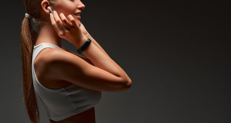 Focused young athlete girl with smart bracelet wearing sportswear putting on earphones. Side view. Copy space. Web banner. Cropped image.の写真素材