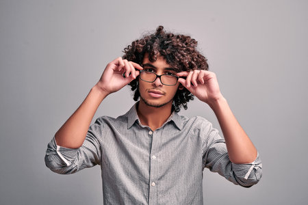 Image on isolated background of young handsome eastern man holding hands on his eyeglasses. Egyptian...
