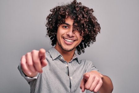 Portrait of handsome smiling arabian man pointing on camera with both hands. Joyful indian boy friendly smiling and gesturing at cameraの写真素材