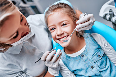 Beautiful kid girl smiling in dentist's chair the office treats teeth. Doctor mask and child looks at camera. Close up viewの写真素材