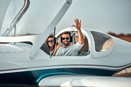Young beautiful man in sunglasses waving from the plane cabin after landing. Side viewの写真素材