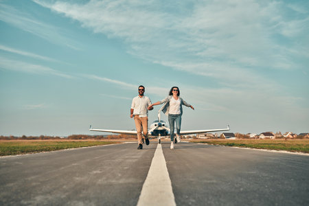 Happy young couple walking from a private airplane walking on runway. Models wearing casual clothes and smiling. Concept is travel on vacation. Copyspaceの写真素材