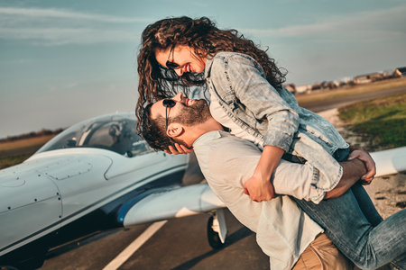 Loving young couple posing on the runway in airport at sunny summer evening. Man holding woman in his arms, models smiling with love and happinessの写真素材