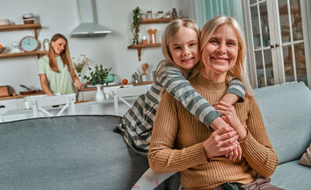 My loving grandmother. The little girl hugs her grandmother and laughs. On the back background mom prepares food.の写真素材