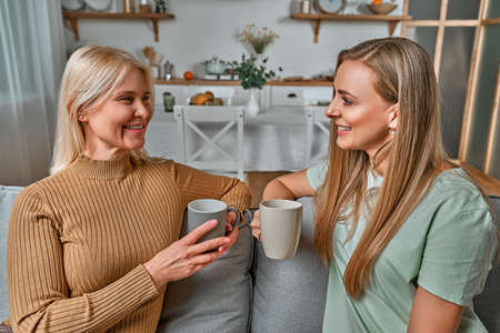 Mom! I can share everything with you! An old mother and her daughter are sitting in the kitchen having a cup of coffee and talking.の写真素材