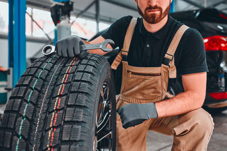 Mechanic holding car tire at garage. Cropped photo. Selective focus.の写真素材