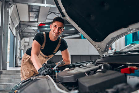 Mechanic working on engine in auto repair shop. Looking at the camera. Selective focus.の写真素材