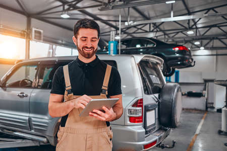 Portrait of young mechanic holding digital tablet in his auto repair shop. Front view.の写真素材
