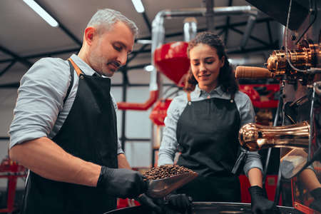 A man and a woman are busy roasting coffee on the background of a roasting machine. The roasting...