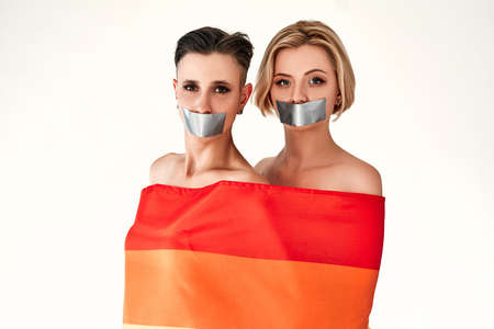 Two women censored with mouth tape wrapped in a rainbow flag. LGBT rights, censorship concept. Isolated white background.の写真素材