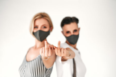 Two women in a medical mask with middle finger fuck sign hand gesture,  protection. Isolated white background. Focus on a hands.の写真素材