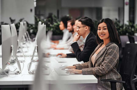 Group of successful smiling business people working on computers together in a spacious office. Data analysis, statistics, finance. Training, business team, programming, development.の写真素材