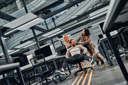Break at work. Young business people have fun and drive on office chairs and laugh.の写真素材