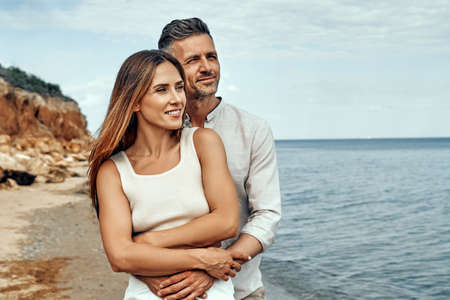 Lovers near the sea hug and have fun. Husband and wife hugs near the sea. lovers on vacation. Summer rest. Romantic walk by the sea. Copy space.の写真素材