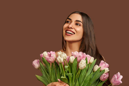 Attractive woman holding a bouquet of white and pink tulips on a brown background laughs and looks up. copyspace.の写真素材