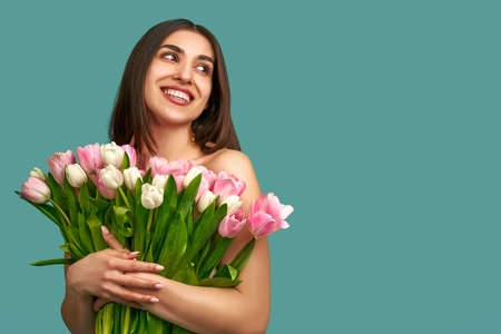 Portrait of a beautiful young woman on a blue background holding a bouquet of white and pink tulips. spring and beauty concept.の写真素材