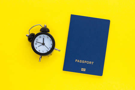 Mini alarm clock and passport on yellow background. Time to travel or vacation. World Tourism Day. Flat lay, top view with copy space.の写真素材
