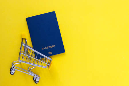 Biometric passports in mini shopping cart on yellow baclground. Business trip and travel, online...