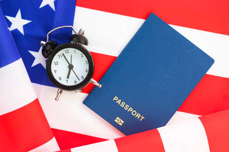 Mini alarm clock and passport on American flag. Journey to USA. Time to travel or vacation. World Tourism Day. Flat lay, top view.の写真素材