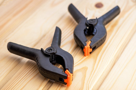 Plastic spring clamps are clamping to glue two pieces of wood. Wooden background. Building equipment. Woodworking hand tool.の写真素材