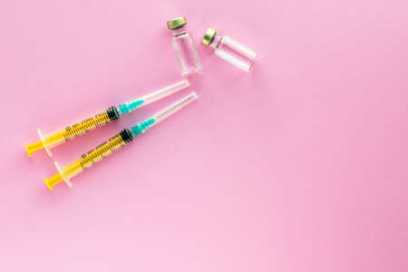 Two syringes and glass vials with liquid on light pink background. Health and vaccination concept. Medical injection. Needle, dosage scale. Top view, flat lay with copy space.の写真素材