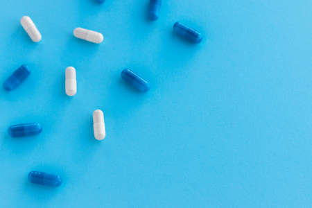 White and blue capsules isolated on light blue background. Epidemic, painkillers, healthcare and treatment concept. Flat lay. Top view with copy space.の写真素材