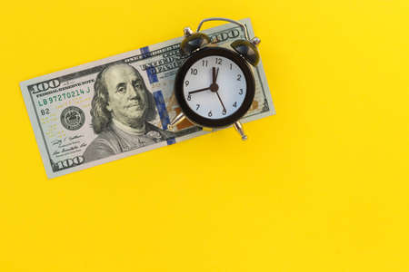 Mini alarm clock and 100 dollars banknote on yellow background.の写真素材