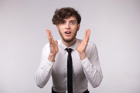 Portrait of young man with shocked emotional facial expression and hands gesture on light gray backgroundの写真素材