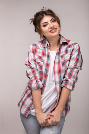 Portrait of a young smiling woman in plaid shirt and white t-shirt, standing over gray wall.の写真素材