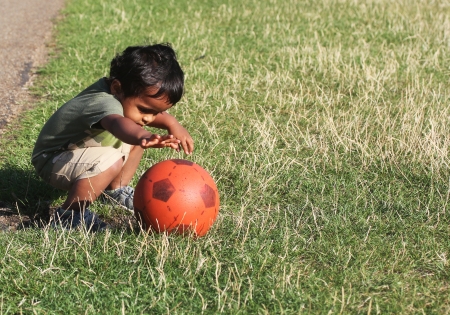 A Young Indian Toddler playing with a red ball in a green grass of a garden or a parkの写真素材