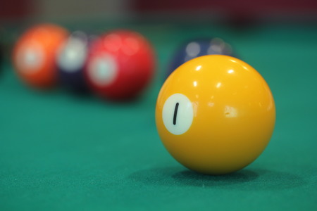 yellow snooker ball with number one on it with other colorful balls placed in a row on a table -...