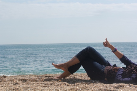 legs of happy young white lady relaxing and enjoying sunshine at the beach with thumbs up hand sign with blue sky and sea water in the backgroundの写真素材