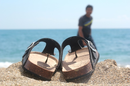 Slippers sandals kept next to sea side with a happy man walking with blue sky and seaの写真素材