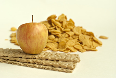 Dietary breakfast. Apple, stack of crispbread and a handful of cornflakes on a light background. Focus on the apple.の写真素材
