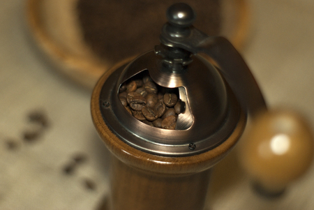 Grains of coffee, poured into a hand grinder, close-up. The handle of the coffee grinder and the background are blurred.の写真素材