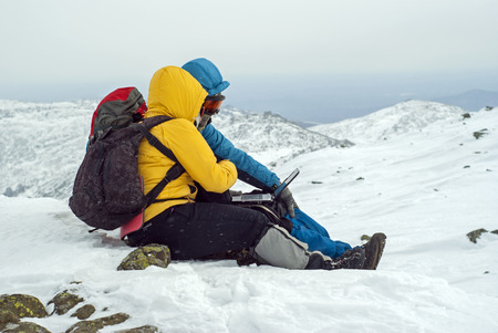 two travelers are sitting with laptop on top of a winter mountain against a background of a blurred highland landscapeのeditorial素材