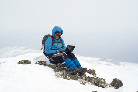traveler working with a laptop in winter on top of a mountain during the snowfallの写真素材