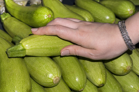 woman buyer chooses zucchini on the counter, only her hand is visibleの写真素材