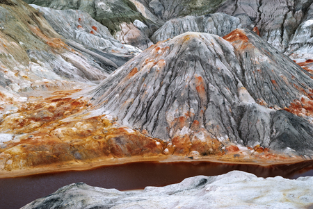 landscape of a multi-colored weathered hilly desert with a poisonous river with red water