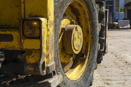 fragment of a heavy worn tractor mounted loader with a huge wheel on a city street during repair...