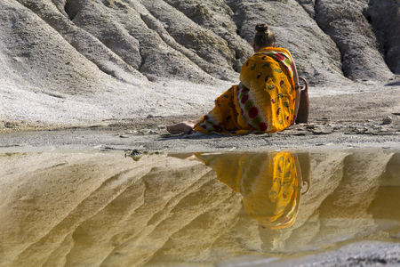 woman in ethnic clothes sitting on the lake shore with her back to the viewerの写真素材